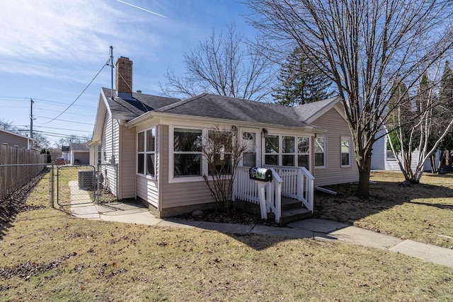 back of house with cooling unit, fence, a shingled roof, a chimney, and a lawn