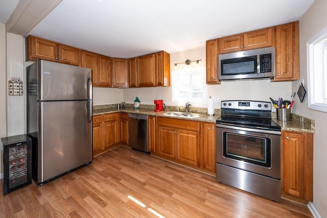 kitchen featuring beverage cooler, brown cabinets, a sink, appliances with stainless steel finishes, and light wood-type flooring