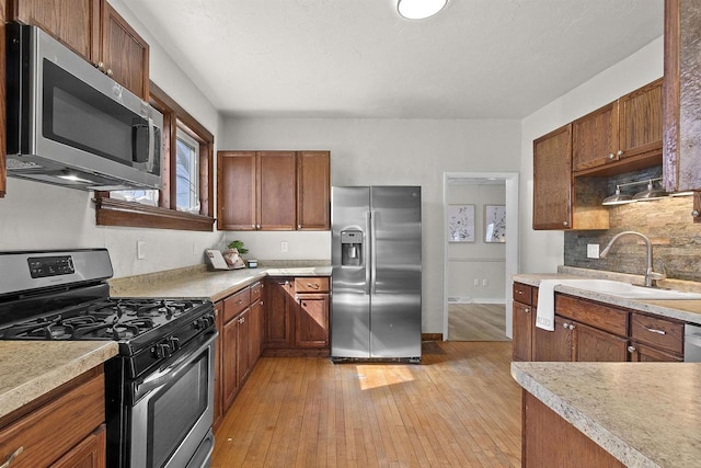 kitchen featuring backsplash, light countertops, light wood-style floors, stainless steel appliances, and a sink