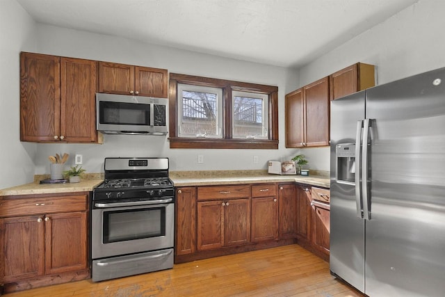 kitchen featuring light wood finished floors, brown cabinetry, appliances with stainless steel finishes, and light countertops