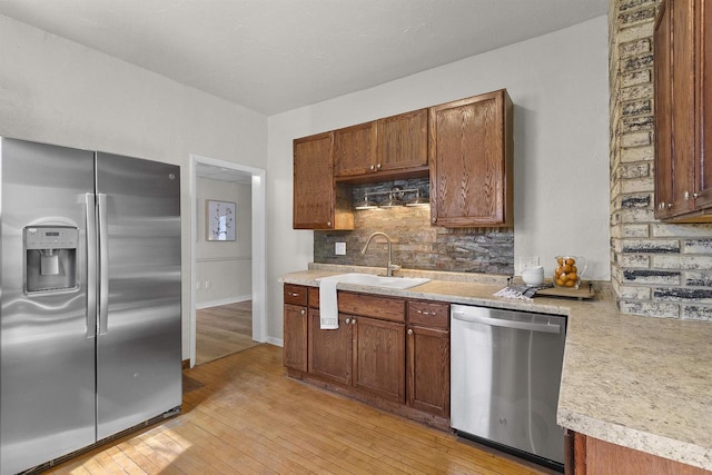 kitchen featuring a sink, stainless steel appliances, light countertops, light wood-type flooring, and backsplash