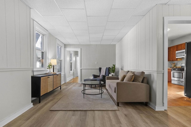 living area with light wood finished floors, a drop ceiling, and baseboards