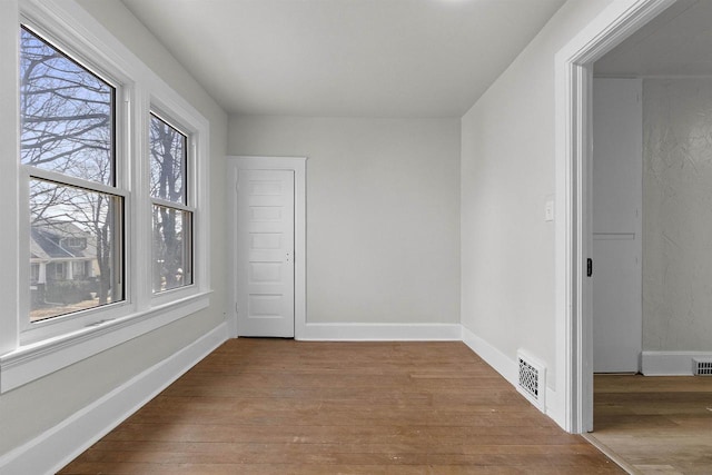 empty room featuring wood finished floors, visible vents, and baseboards