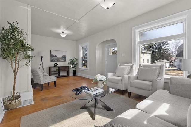 living room with wood finished floors, arched walkways, and baseboards