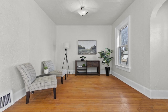 living area featuring baseboards, visible vents, light wood finished floors, arched walkways, and a textured wall