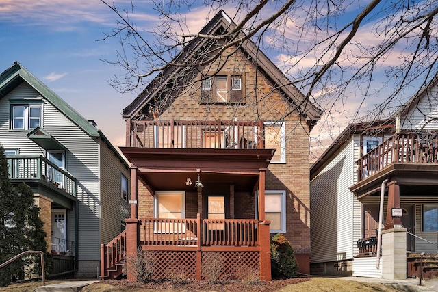 view of front facade featuring brick siding, covered porch, and a balcony