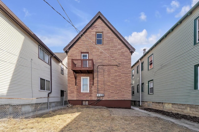 back of house with brick siding, a balcony, and fence