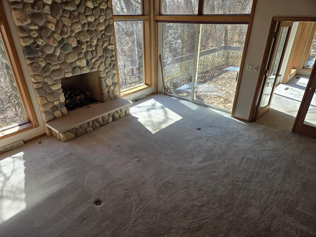 unfurnished living room featuring carpet flooring, a stone fireplace, and visible vents