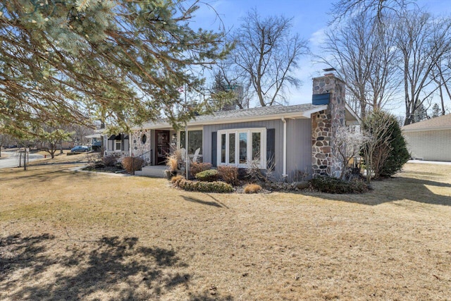 back of house with a yard, stone siding, and a chimney