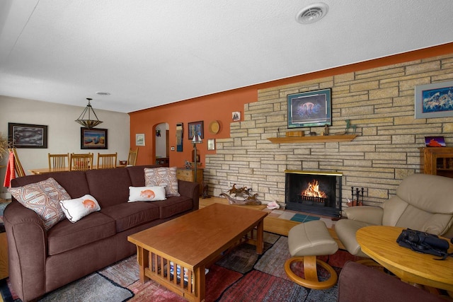 living area featuring arched walkways, visible vents, a fireplace, and a textured ceiling