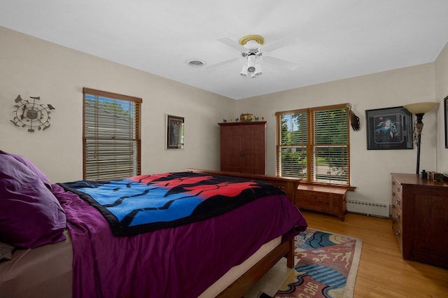 bedroom with light wood finished floors, a ceiling fan, visible vents, and baseboard heating