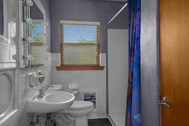 bathroom with curtained shower, tile walls, toilet, and a sink