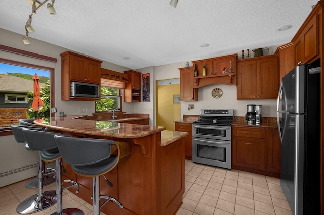 kitchen with light tile patterned floors, light stone countertops, a peninsula, appliances with stainless steel finishes, and a textured ceiling