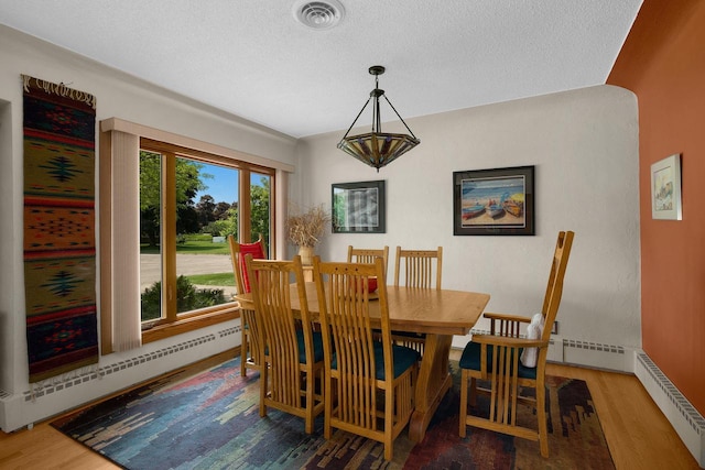 dining space with a baseboard heating unit, wood finished floors, visible vents, and a textured ceiling