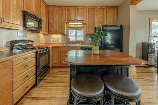 kitchen with a breakfast bar, a healthy amount of sunlight, black appliances, and a sink