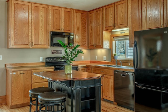 kitchen featuring black appliances, a sink, wood counters, a kitchen breakfast bar, and light wood finished floors