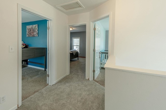 hall featuring baseboards, carpet, and attic access