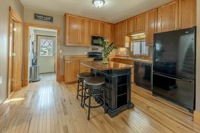 kitchen featuring a kitchen bar, black appliances, light wood-style flooring, and a center island