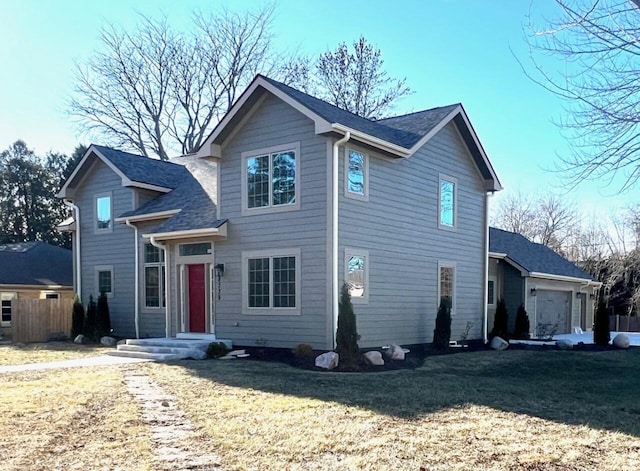 traditional-style home with an attached garage, roof with shingles, a front lawn, and fence