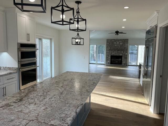 kitchen featuring dark wood-style floors, a stone fireplace, white cabinets, and double oven