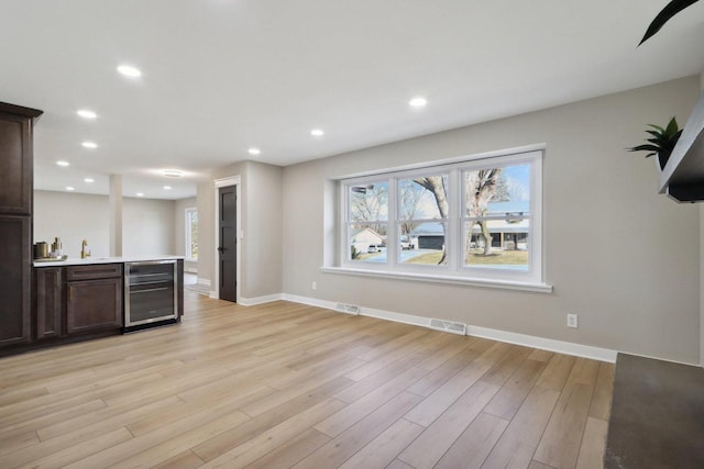 kitchen featuring light wood finished floors, visible vents, dark brown cabinets, beverage cooler, and light countertops