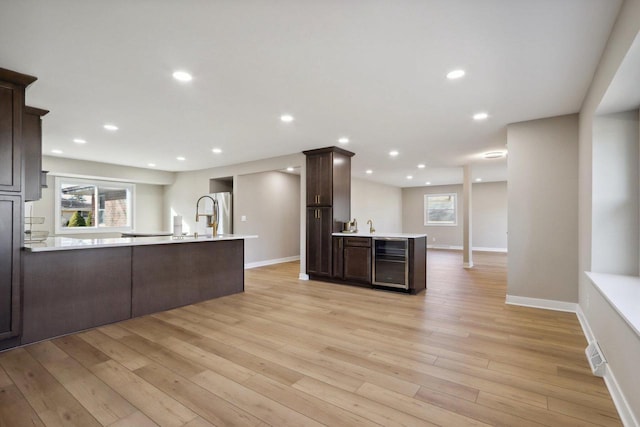 kitchen with beverage cooler, a peninsula, light wood-style flooring, light countertops, and dark brown cabinetry