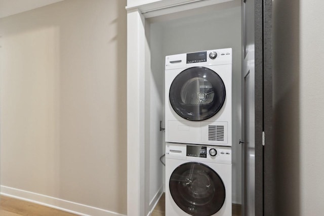 laundry room with baseboards, stacked washer and clothes dryer, wood finished floors, and laundry area