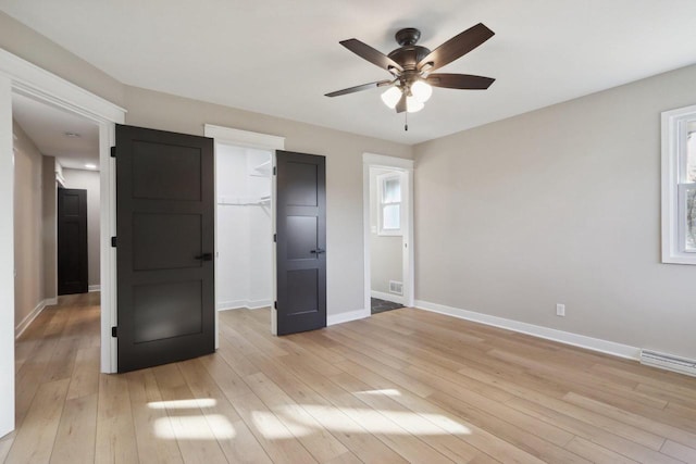 unfurnished bedroom with a closet, a walk in closet, light wood-type flooring, and baseboards