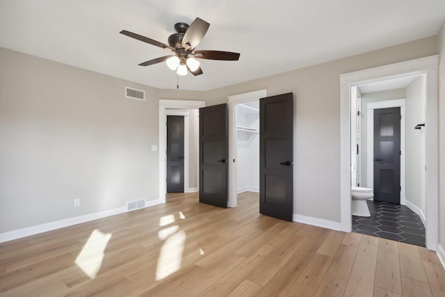 unfurnished bedroom featuring light wood finished floors, visible vents, a walk in closet, and baseboards