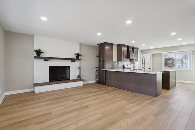 kitchen with light wood-type flooring, wall chimney range hood, a peninsula, light countertops, and dark brown cabinets