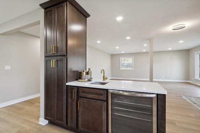 kitchen with beverage cooler, dark brown cabinetry, light wood-style floors, and a sink