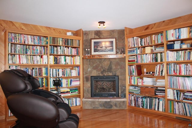 living area with wall of books, wood finished floors, and a fireplace