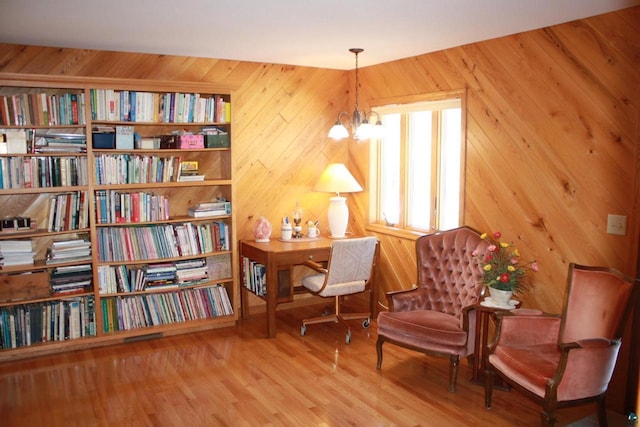 sitting room with wooden walls, an inviting chandelier, and wood finished floors