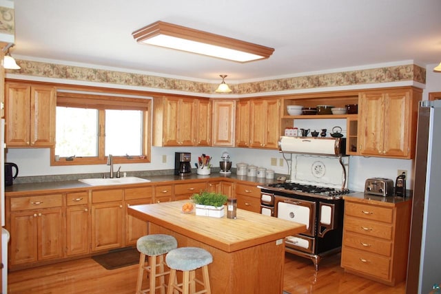 kitchen with range with gas stovetop, light wood finished floors, wooden counters, freestanding refrigerator, and a sink