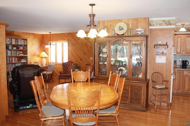 dining area with a chandelier, wooden walls, and light wood-type flooring