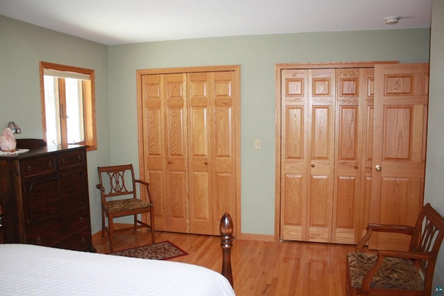 bedroom featuring light wood-type flooring, baseboards, and two closets