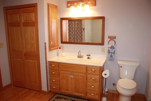 bathroom featuring toilet, vanity, baseboards, and wood finished floors