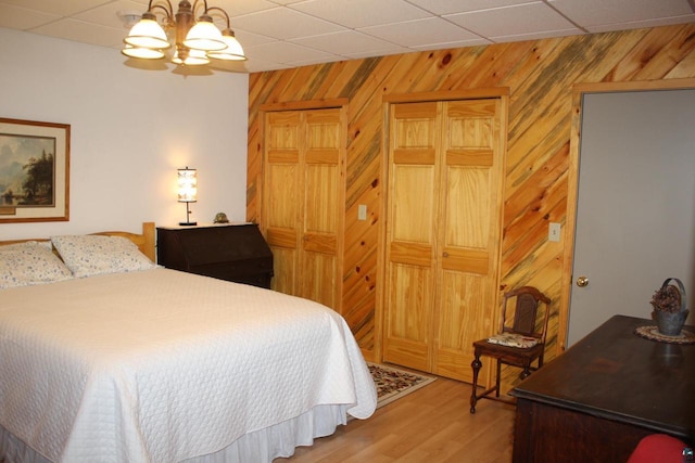 bedroom featuring a paneled ceiling, wooden walls, and wood finished floors