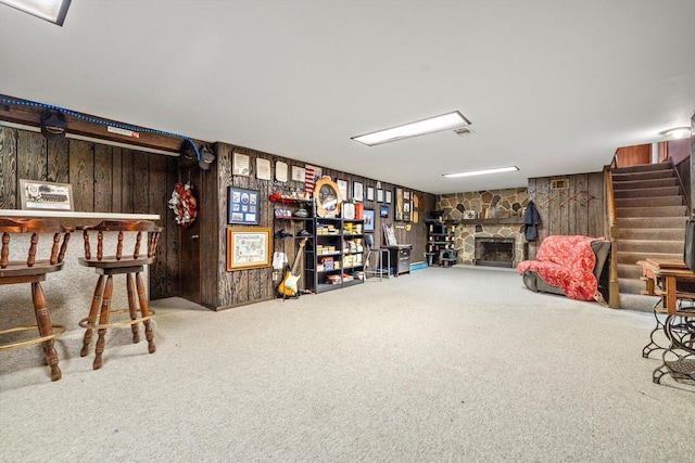 finished below grade area with stairs, a stone fireplace, wooden walls, and carpet floors