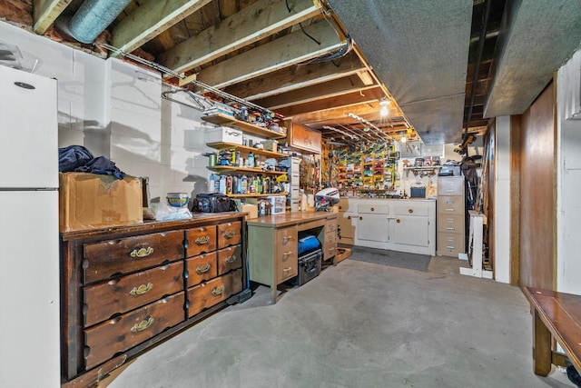 unfinished basement featuring a workshop area and freestanding refrigerator