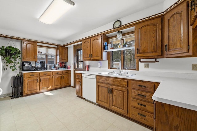 kitchen featuring brown cabinetry, dishwasher, light countertops, and a sink