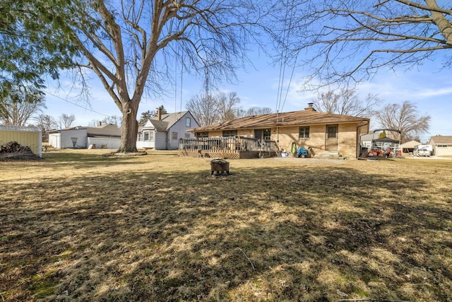 rear view of house featuring brick siding, an outdoor fire pit, a wooden deck, a lawn, and a chimney