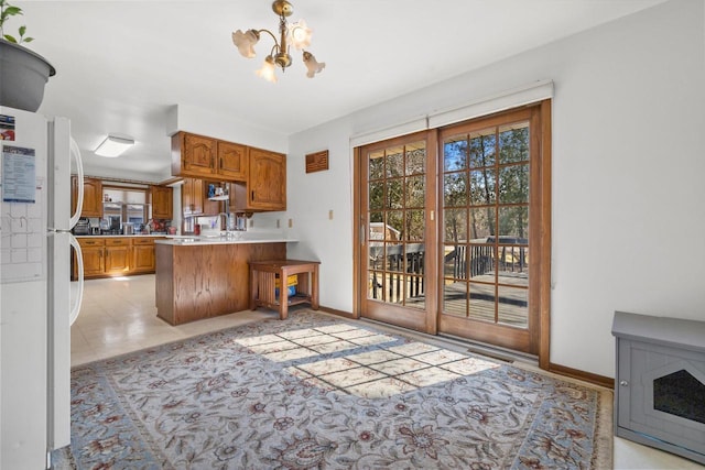 kitchen with a peninsula, a notable chandelier, brown cabinetry, and freestanding refrigerator