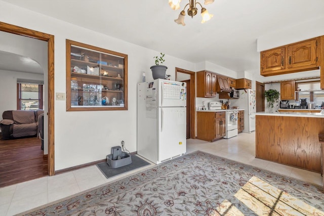 kitchen with brown cabinets, white appliances, arched walkways, light countertops, and light tile patterned floors