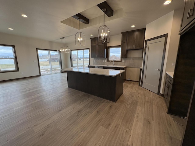 kitchen with light countertops, a chandelier, decorative backsplash, a kitchen island, and dark brown cabinets