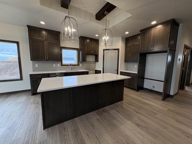 kitchen with light countertops, dark brown cabinets, tasteful backsplash, a sink, and an inviting chandelier