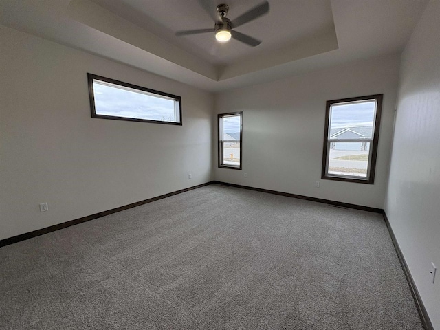 unfurnished room with baseboards, light colored carpet, a ceiling fan, and a raised ceiling
