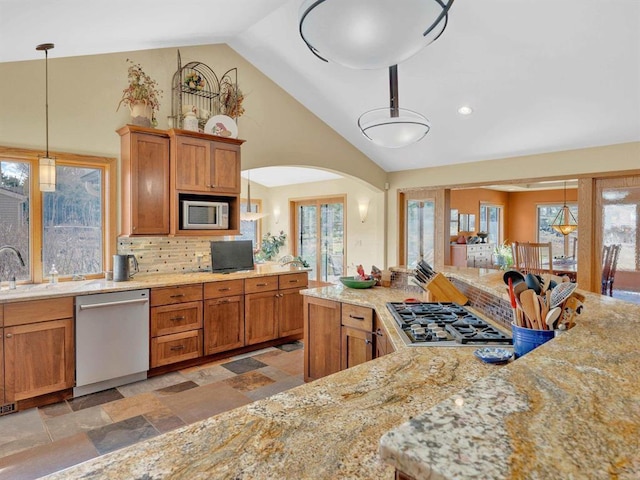 kitchen with stone tile floors, brown cabinetry, arched walkways, and stainless steel appliances