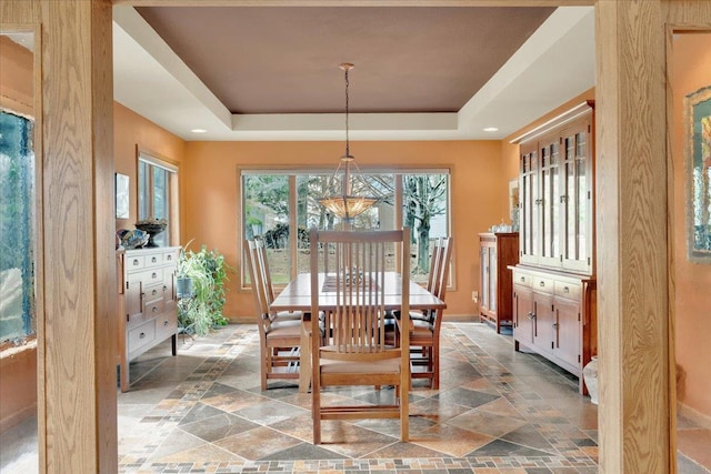 dining room featuring a tray ceiling, baseboards, and stone tile floors