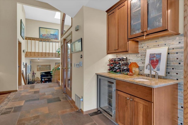 kitchen with a sink, glass insert cabinets, wine cooler, brown cabinetry, and decorative backsplash